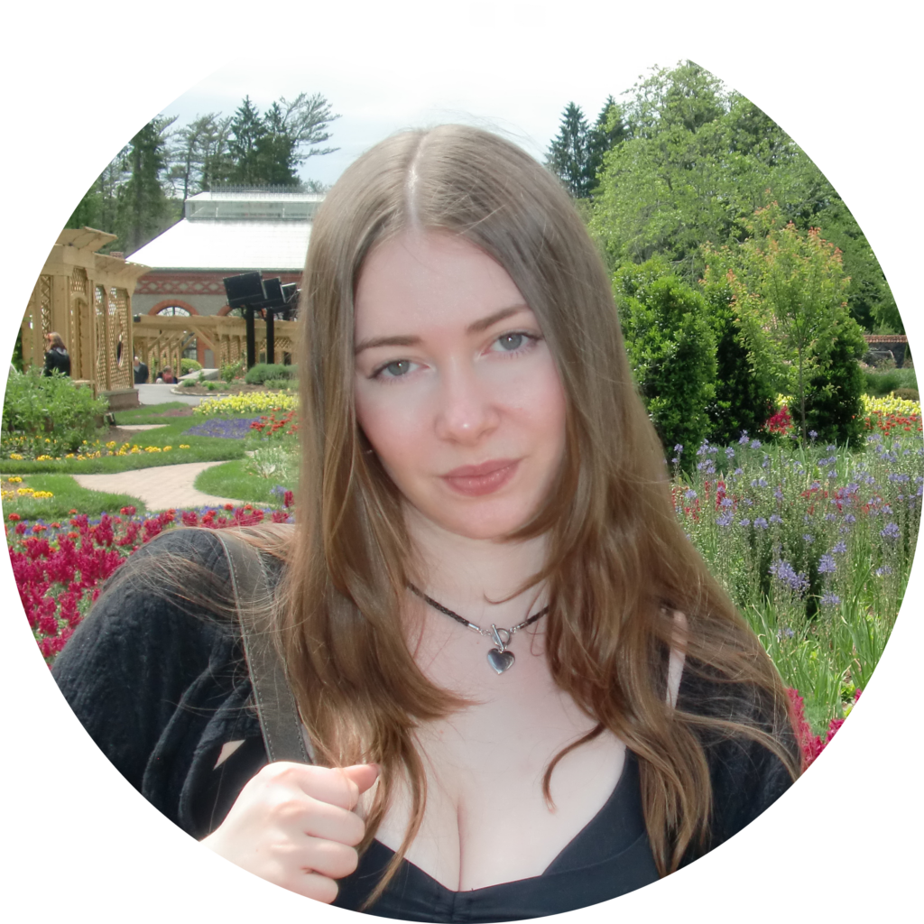 A girl with light brown hair wearing a black shirt, in a flower field. 